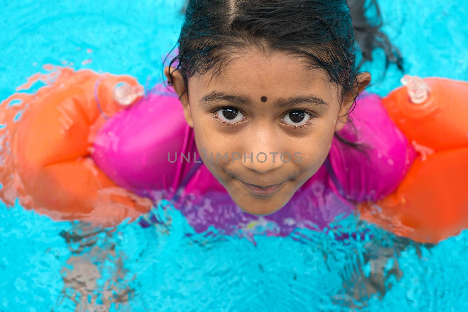 Indian child learning swimming in pool. Asian girl in swimmer class with float bands.