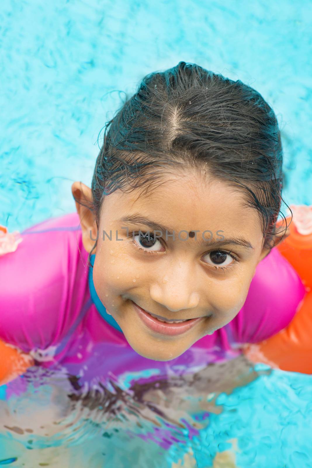 Asian kid in swimmer class with float bands. Indian child learning swimming in pool.