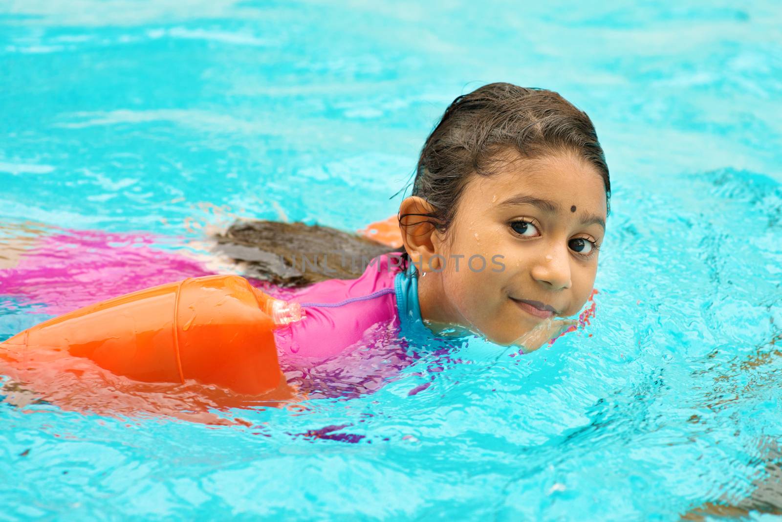 Asian girl in swimmer class with float bands. Indian child learning swimming in pool.