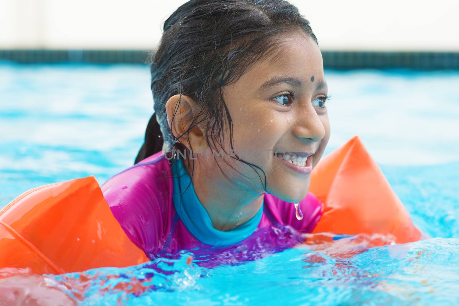 Indian girl learning swimming in pool. Asian child in swimmer class with float bands.