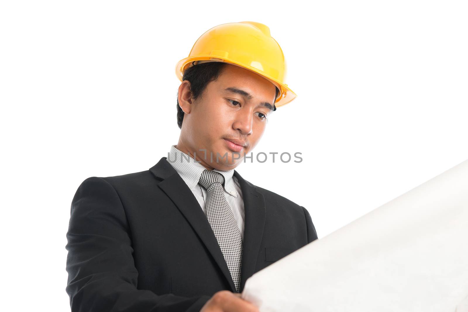 Close-up of an Asian young man wearing a hardhat looking at blueprint paper, standing isolated on white background.