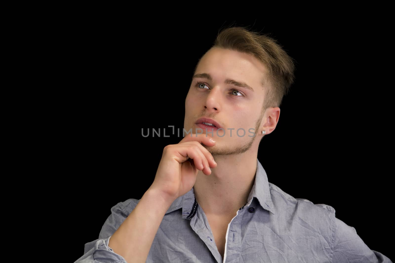 Attractive young man thinking, looking up with hand on his chin, isolated on black background