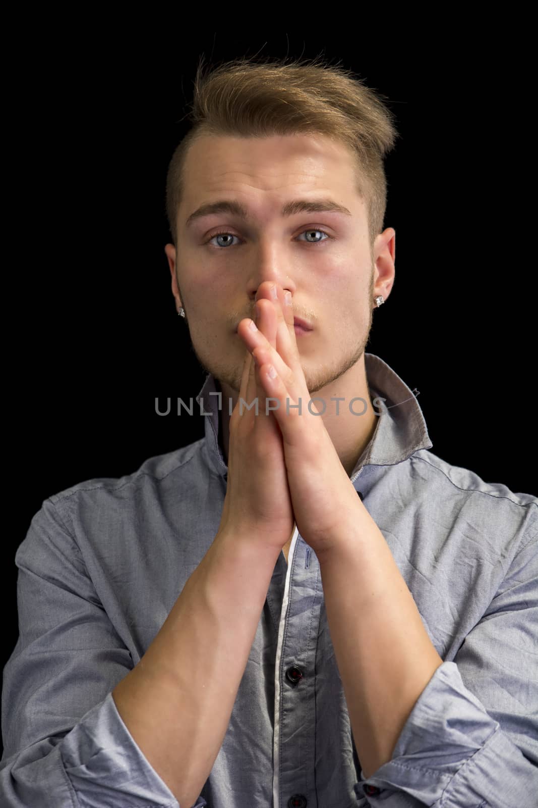 Attractive blond young man, serious expression with hands joined in front of mouth