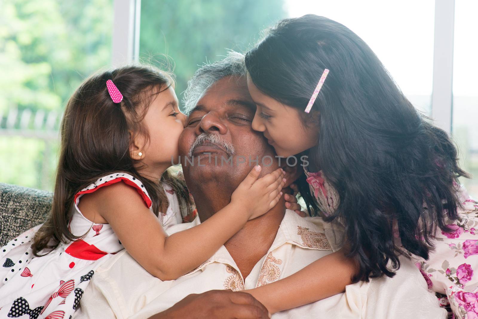 Portrait Indian family at home. Grandchildren kissing on grandparent face. Asian people living lifestyle.