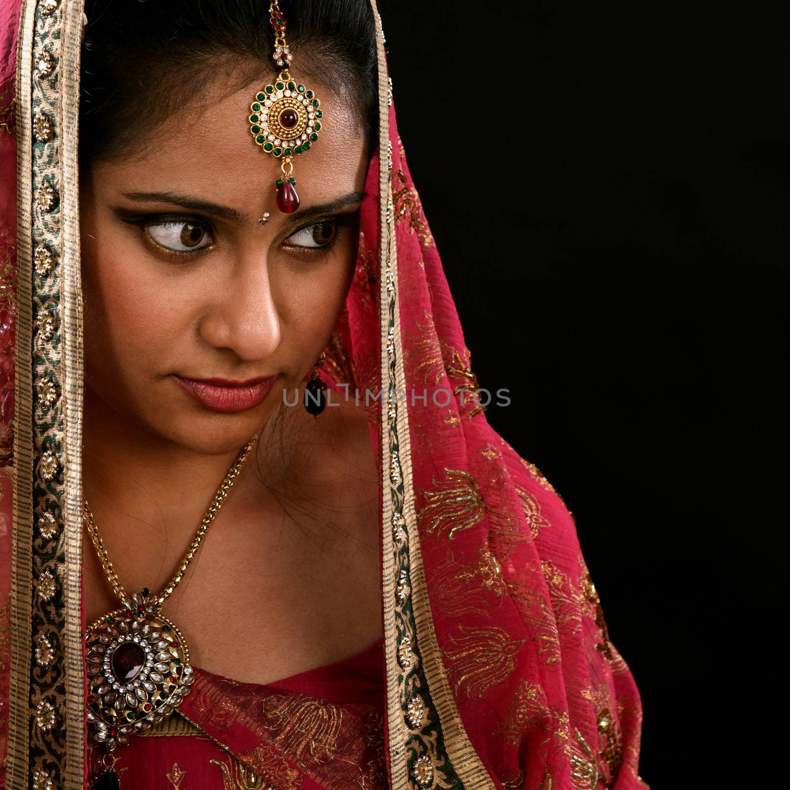Portrait of beautiful young Indian girl looking to copy space at side, isolated on black background.
