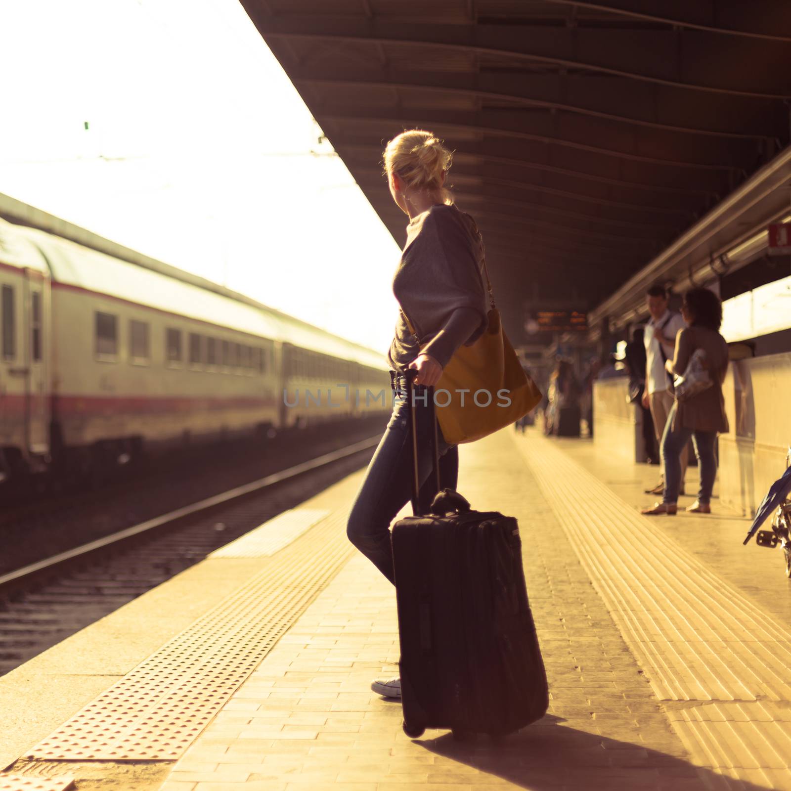 Blonde caucasian woman waiting at the railway station with a suitcase.