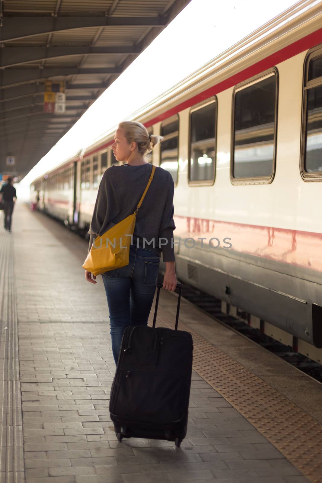 Blonde caucasian woman waiting at the railway station with a suitcase.