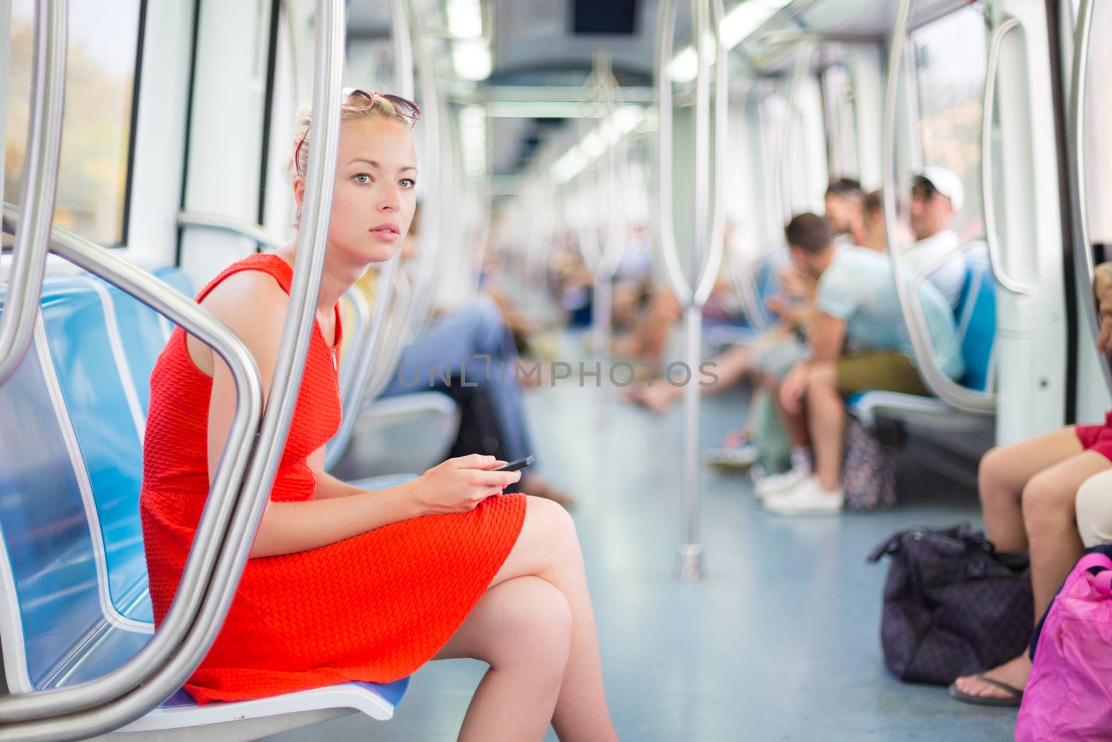 Beautiful blonde caucasian lady in red dress traveling by metro.