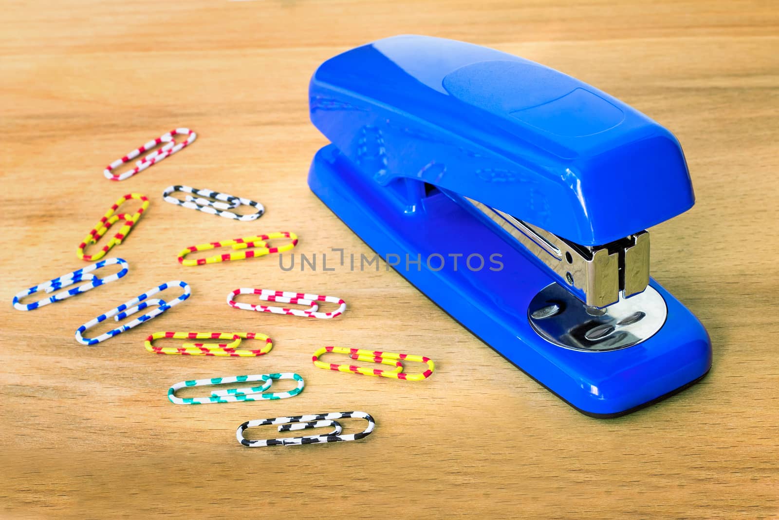 Bright the blue stapler and multi-colored paper clips lie on a table.