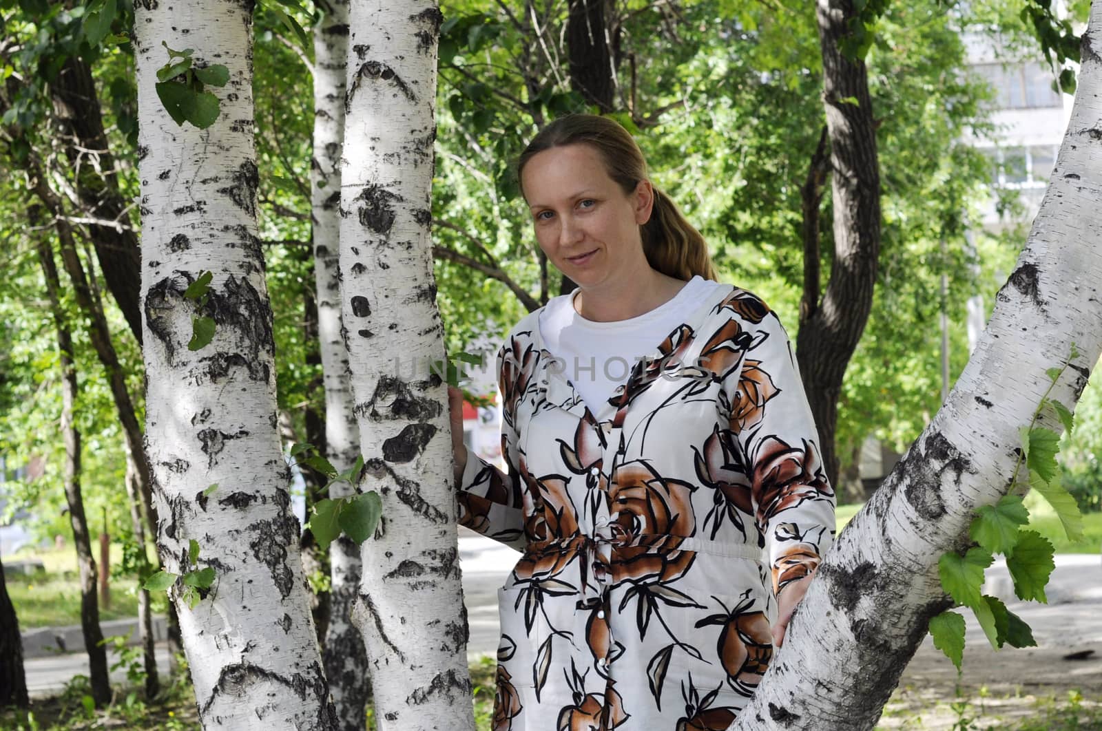 The happy woman stands near birches in park