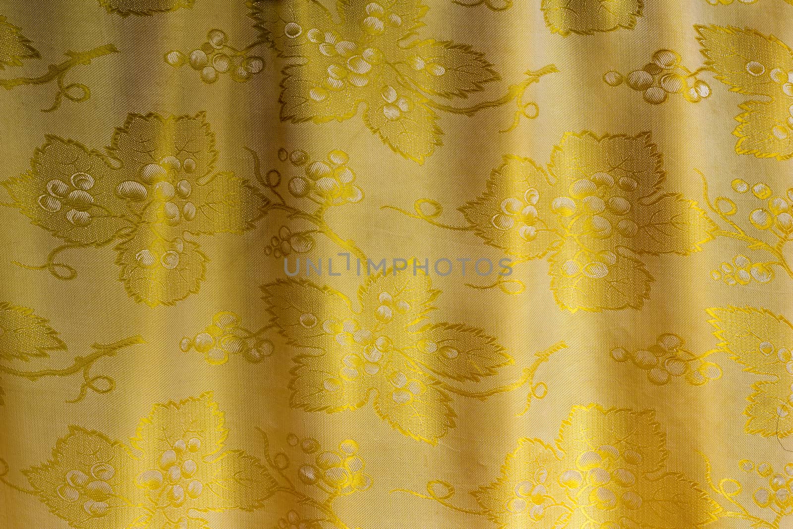  Beautifully draped silk fabric of golden color with an ornament. . It is presented as the background image.