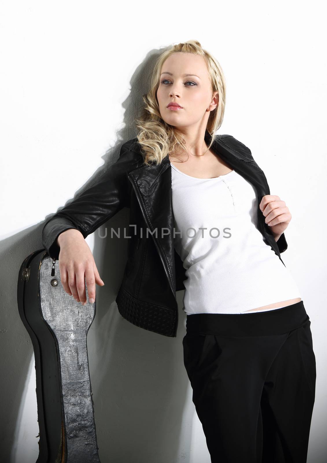 Young woman in a rock band styling is leaning against the wall based on the leather guitar case