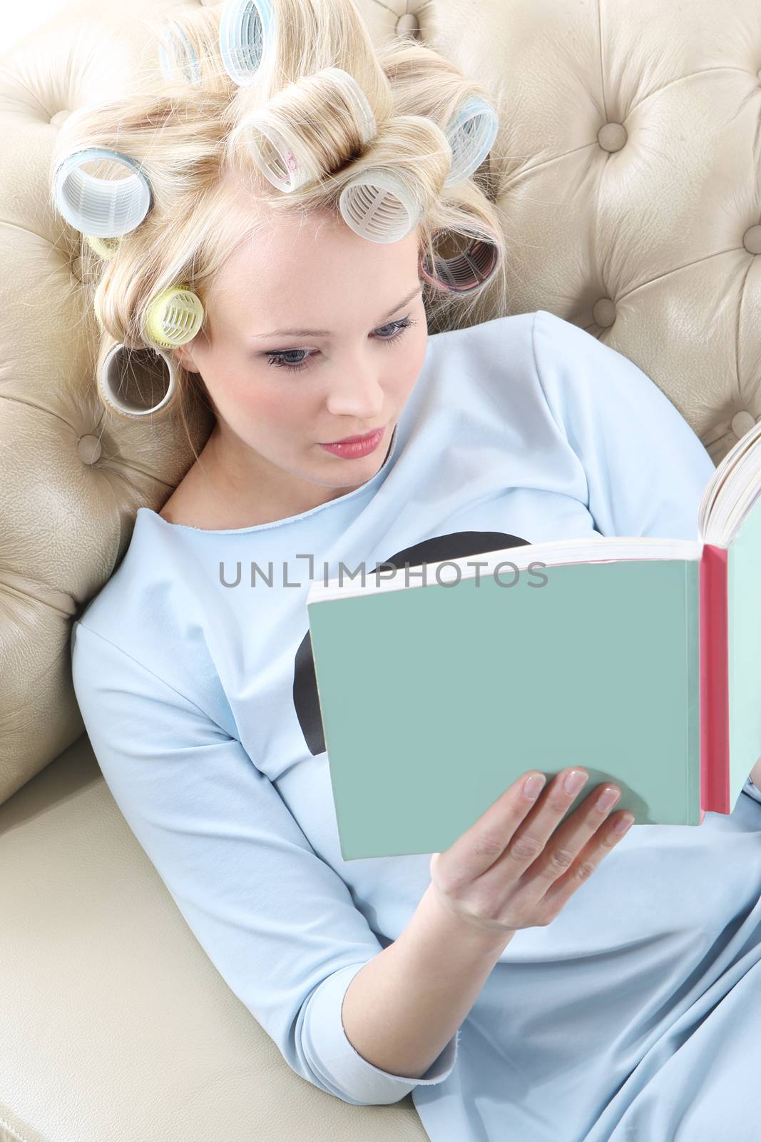 Young woman with hair rollers screwed reading a book while relaxing on the sofa