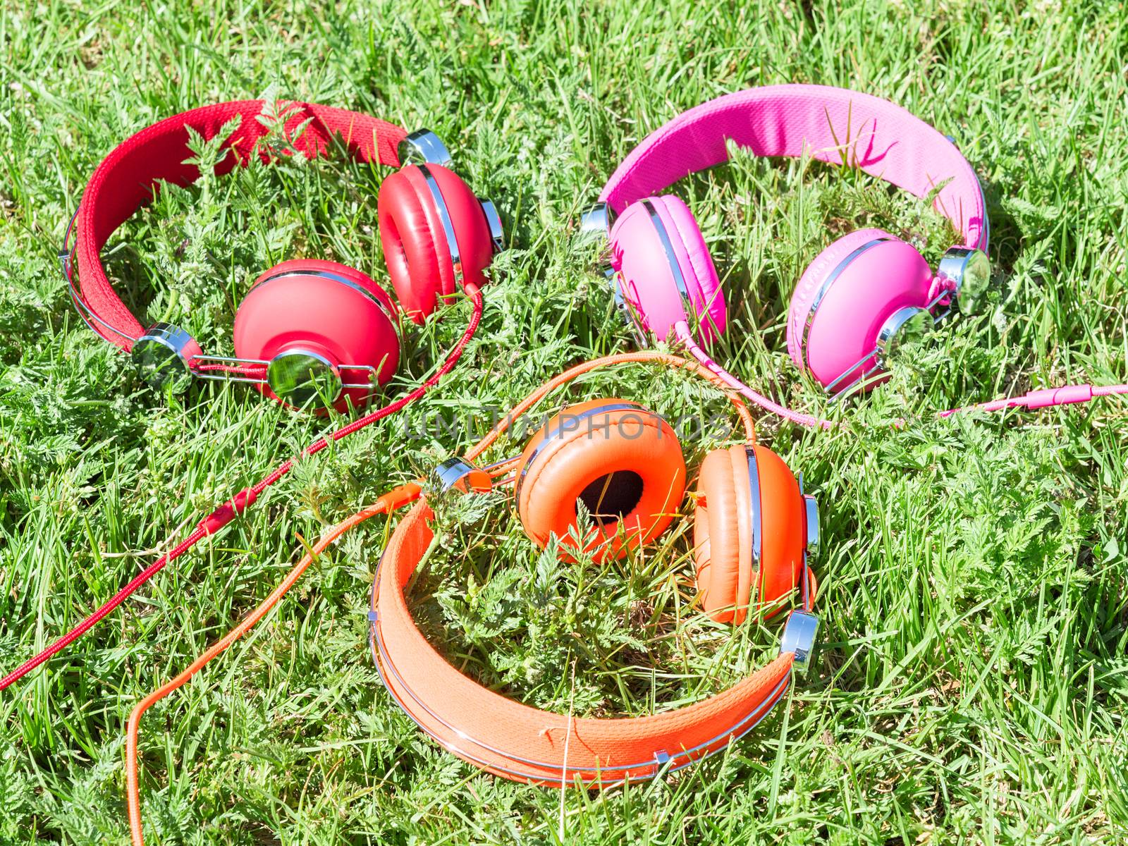 Set of three varicolored colorful headphones on sunlight fresh green sward