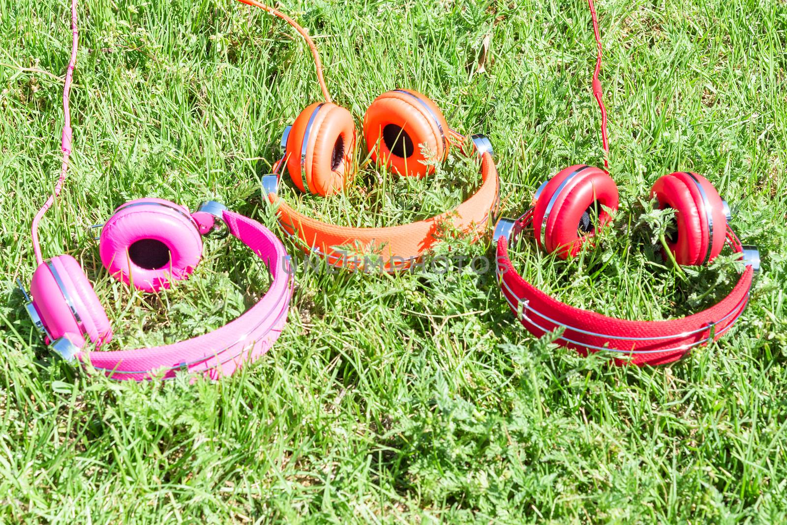 Multicolored kit for mobile mp3 audio entertainment of three vivid colored headphones on summer sunny glade