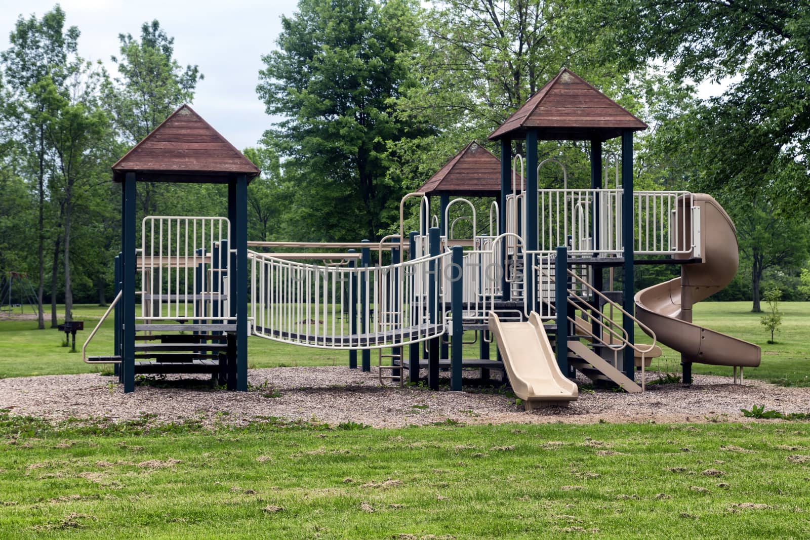 Large green and beige playground. Roofed stuctures, slides, and railed bridges.