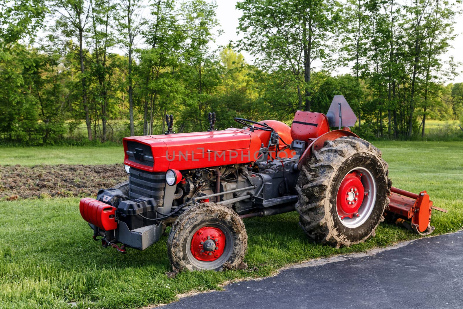 Red tractor with cultivator attached. Parked after just finishing a garden. 