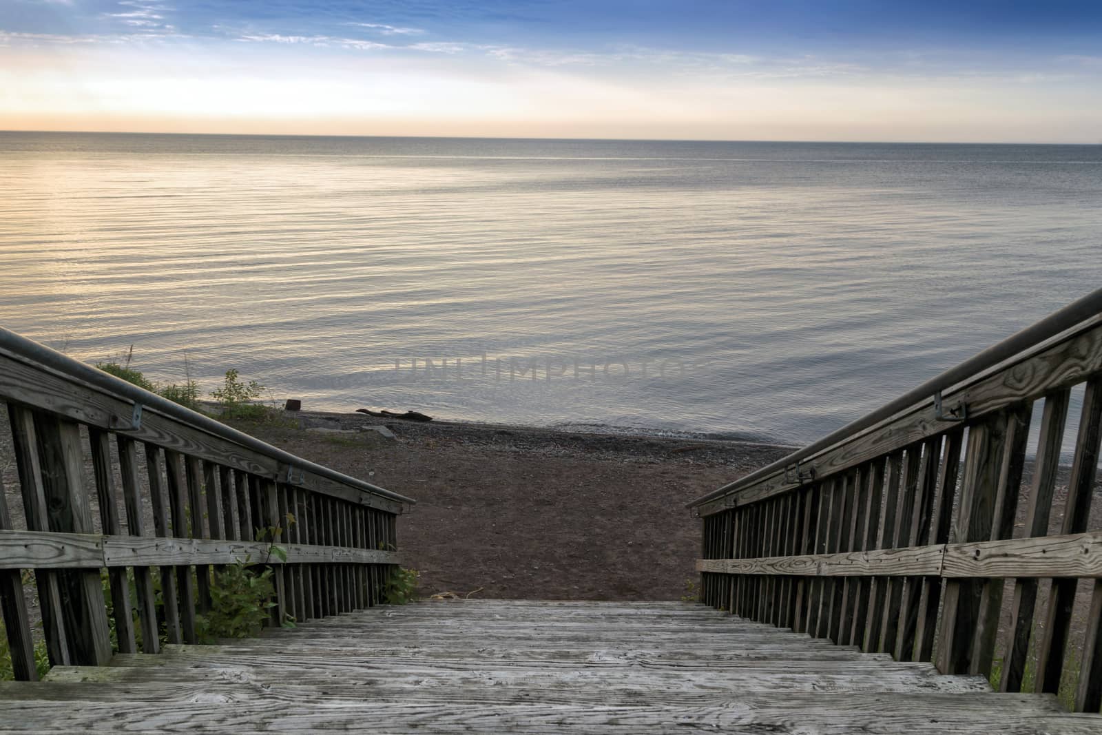 Wide wooden stairway to small beach on the lakefront. Calm water and sky in the background.