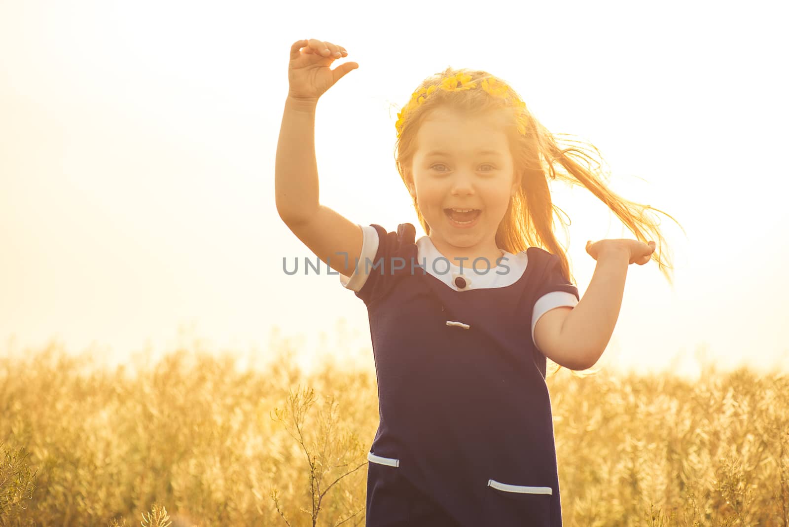 the beautiful little girl in a blue dress laughs, raising hands up