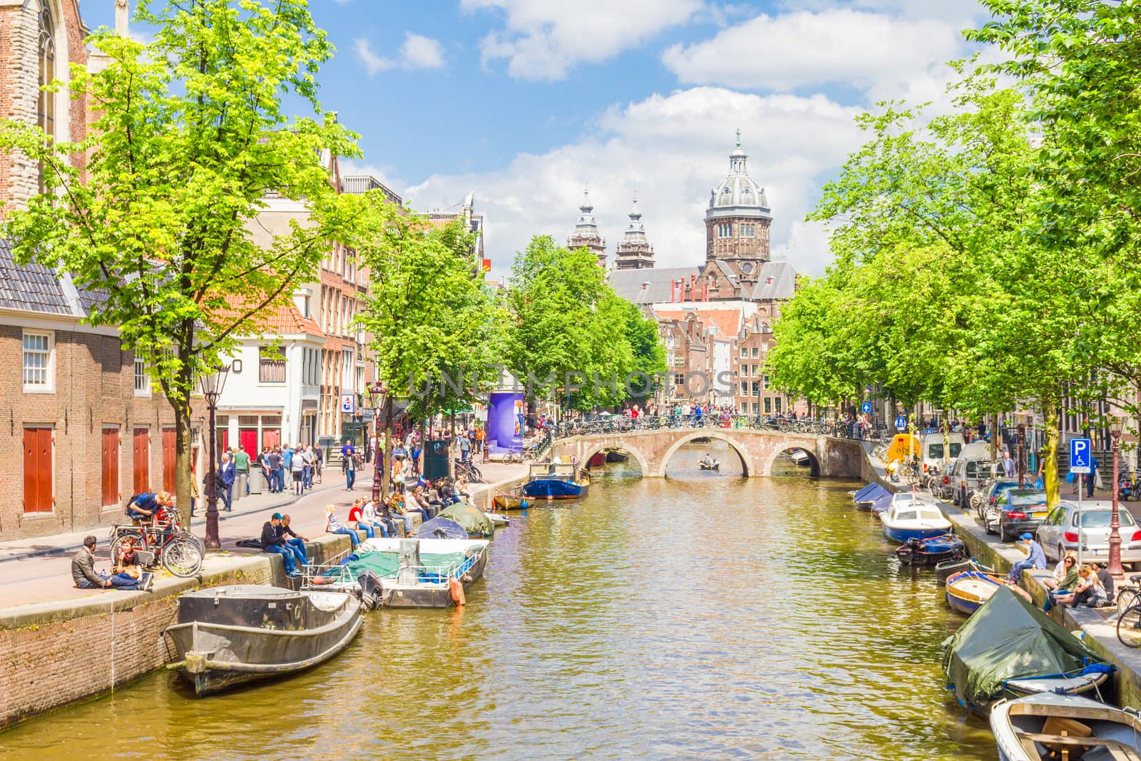 Tourists walking by a canal in Amsterdam. Amsterdam is the capital of the Netherlands and the canals and harbours fill a full quarter of the city surface.