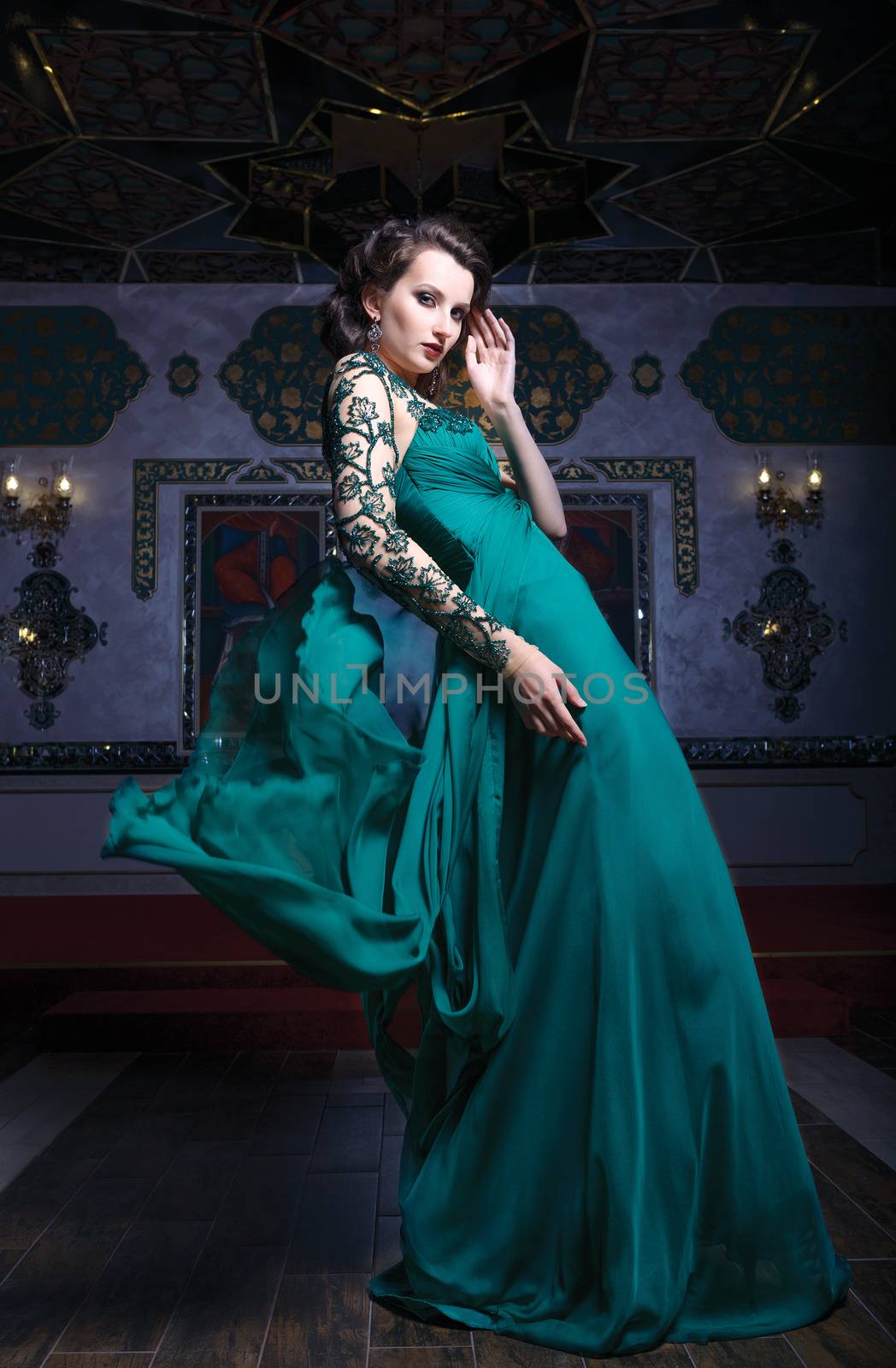 Beautiful woman in a green long dress on a background of richly decorated room