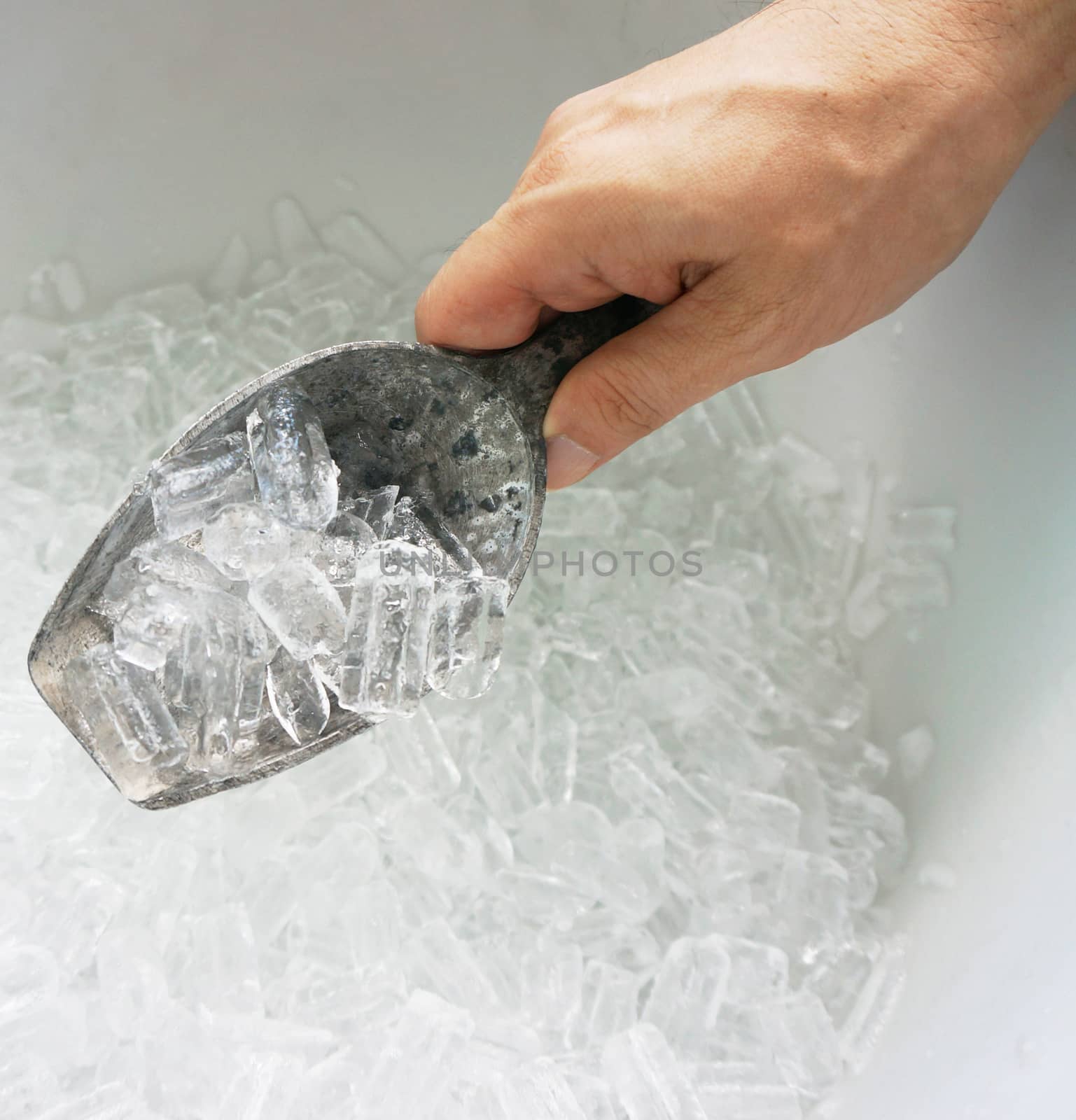 Hand of man is holding the ice scoop, in a cooler packed with ice.                                