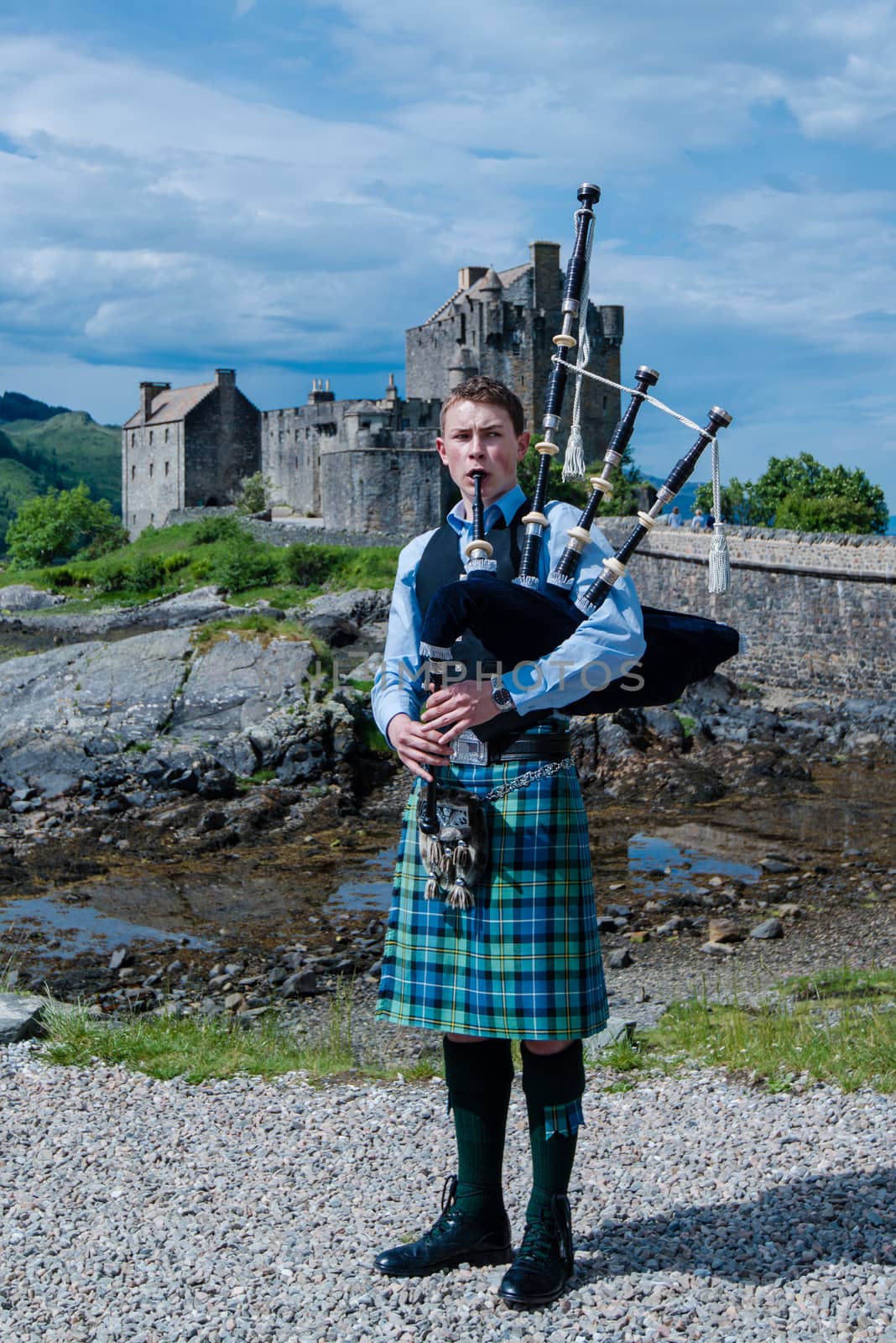 DORNIE, SCOTLAND - June 7, 2014: A bagpipe player with traditional kilt in front of Eilean Donan, the most famous castle in Scotland, on June 7, 2014 in Dornie, Scotland, United Kingdom.