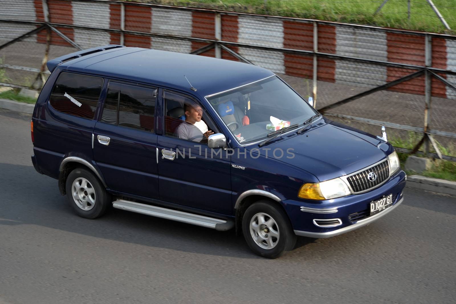 bandung, indonesia-june 16, 2014: blue colored toyota kijang EFI cruising on the road.