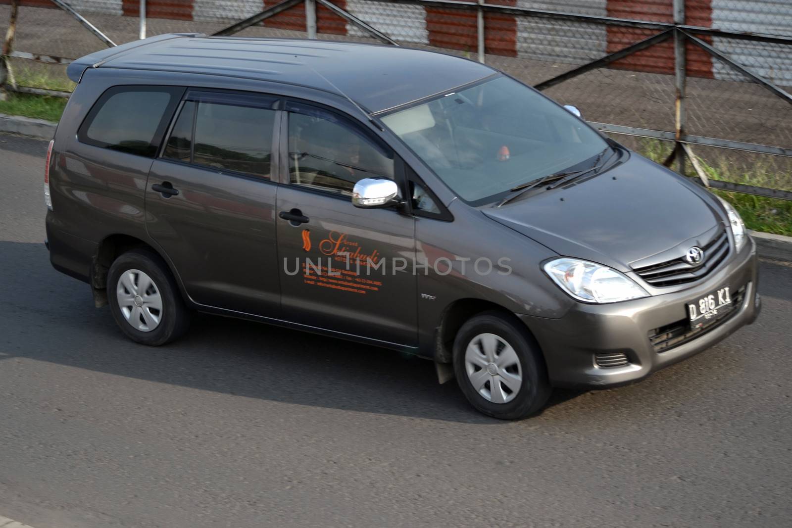 bandung, indonesia-june 16, 2014: grey colored toyota kijang innova cruising on the road.