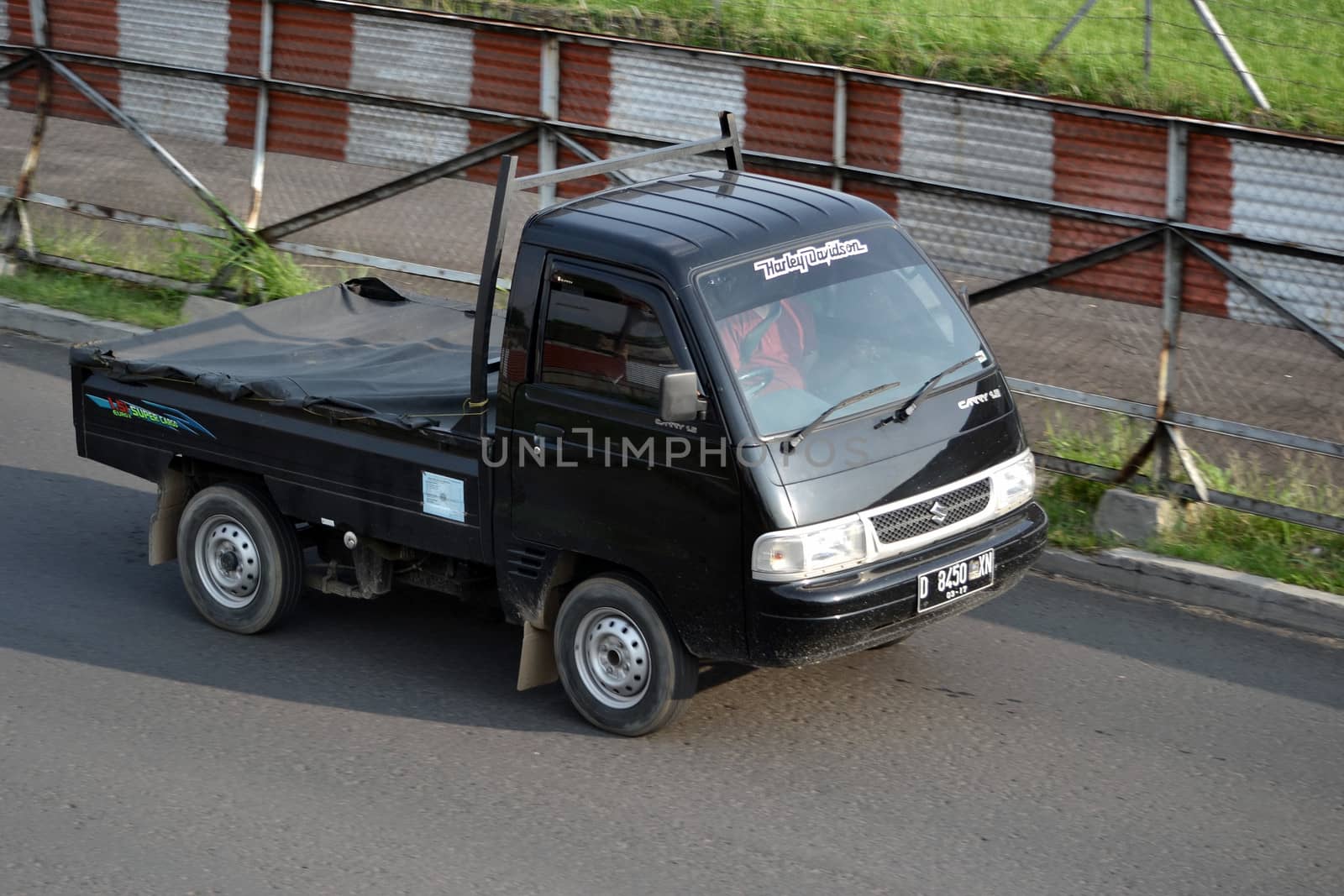 bandung, indonesia-june 16, 2014: black colored suzuki carry cruising on the road.