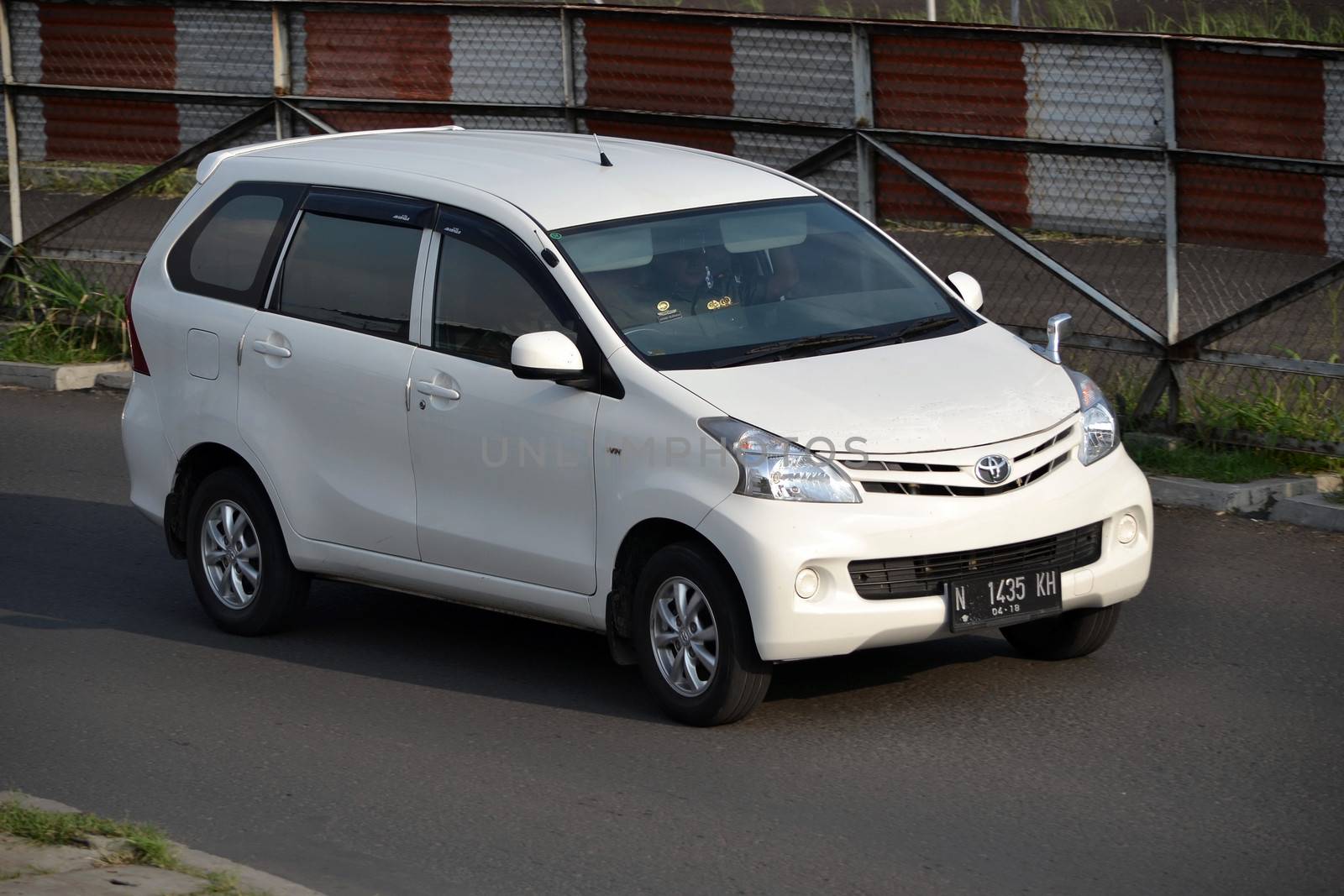 bandung, indonesia-june 16, 2014: white colored toyota avanza cruising on the road.