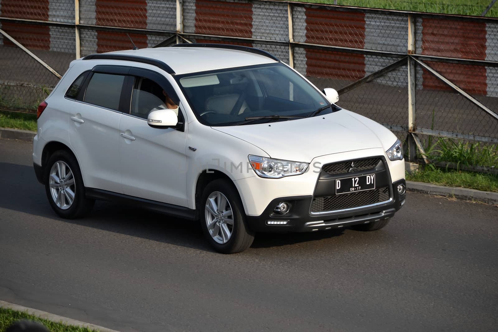 bandung, indonesia-june 16, 2014: white colored mitsubishi outlander sport cruising on the road.