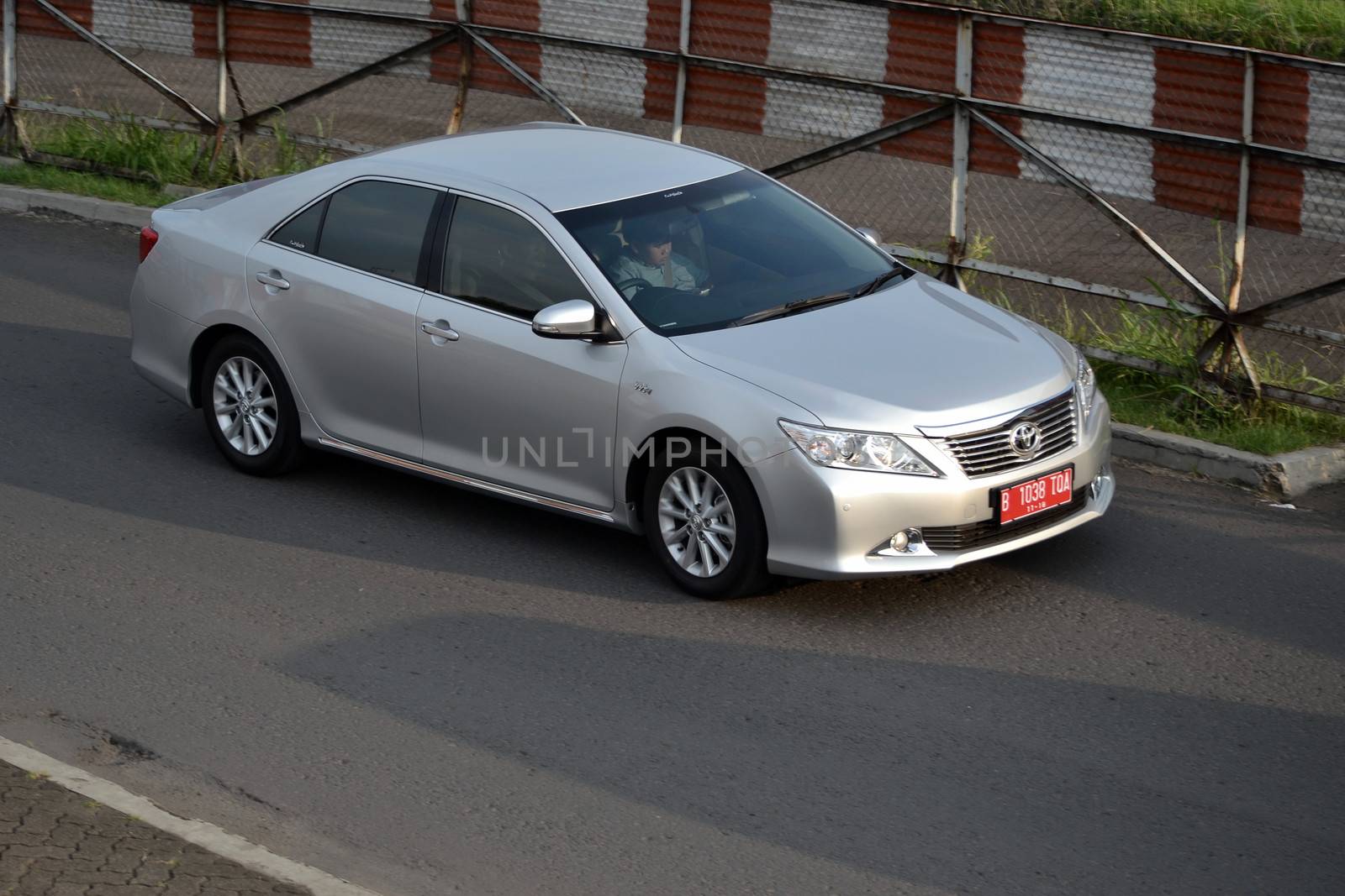 bandung, indonesia-june 16, 2014: silver colored toyota camry cruising on the road.