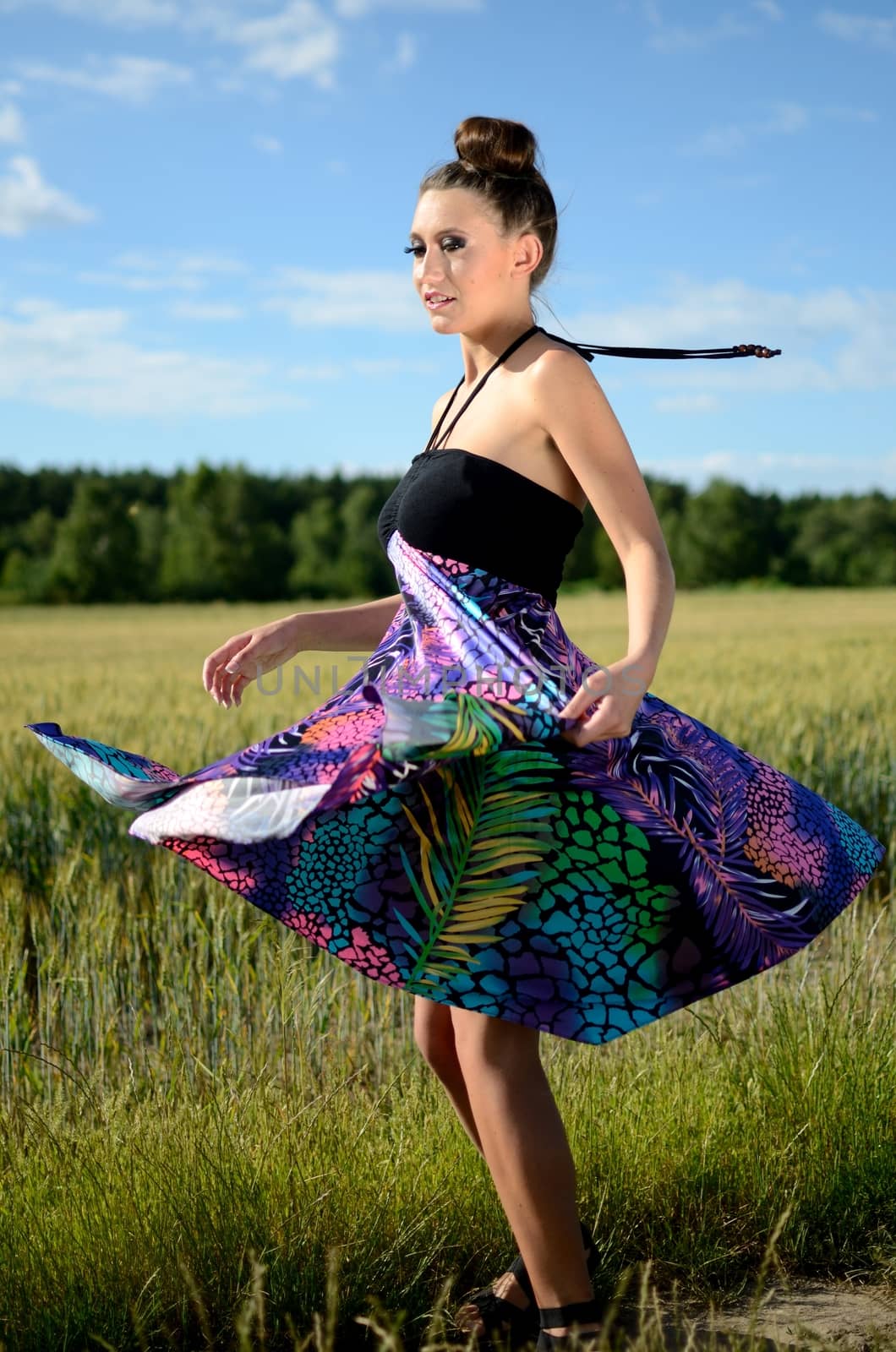 Young female model spins around. Charming girl from Poland, dynamic photo with colorful dress. Green fields and blue sky as background.