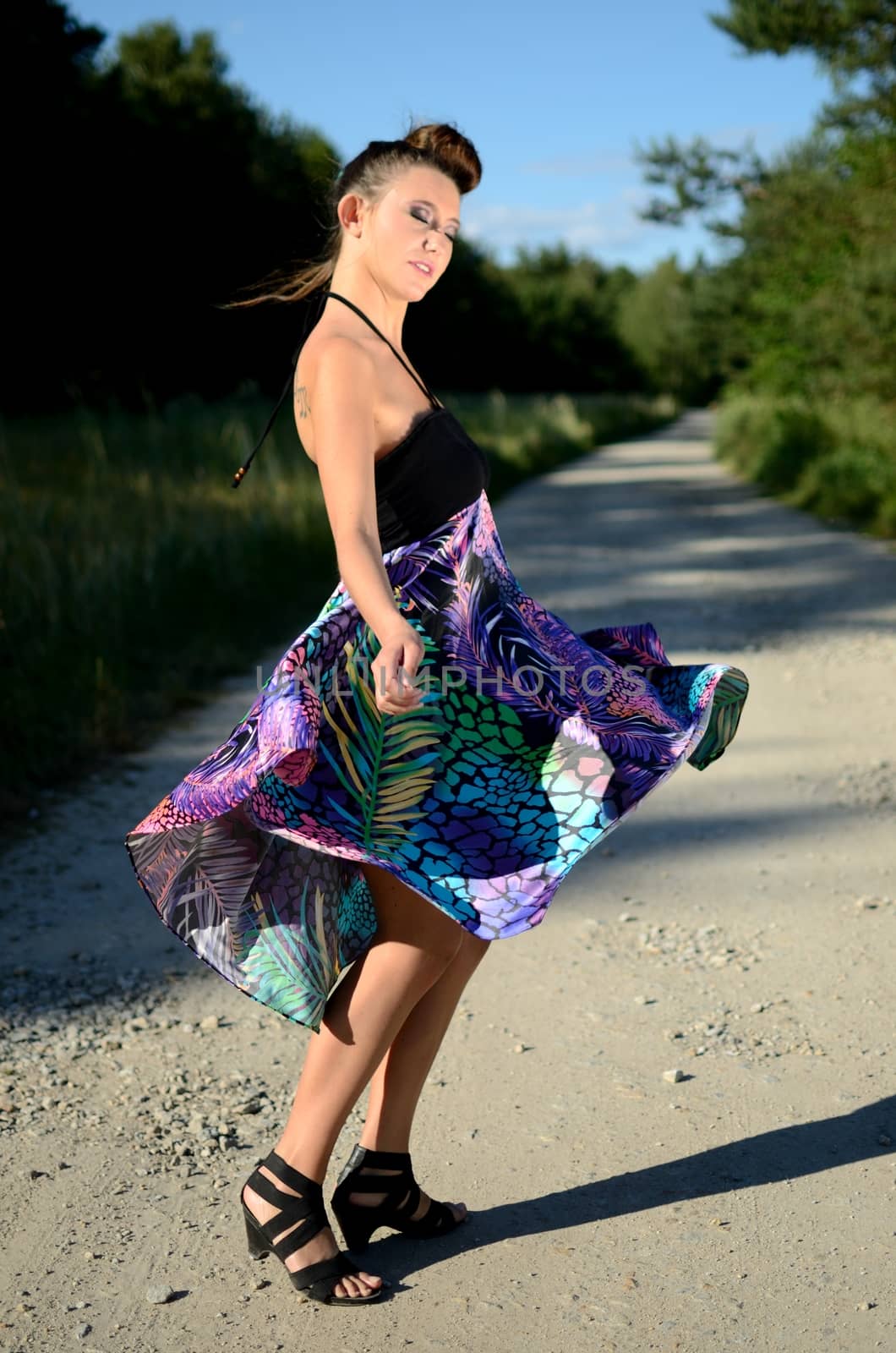 Girl with colorful dress spins around. Female model from Poland with road and forest as background.