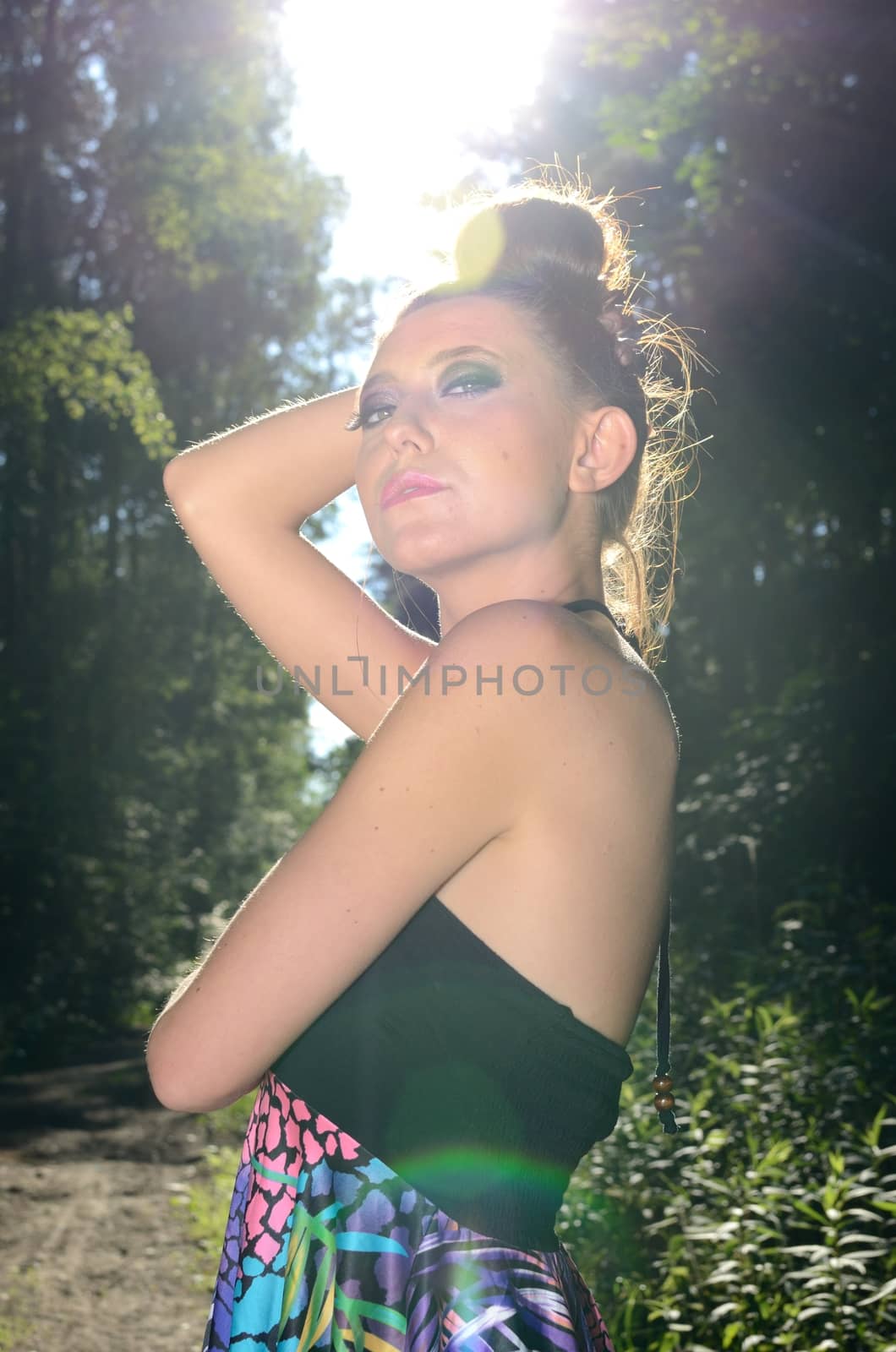 Teenager model portrait. Young female from Poland stands in forest with strong sunlight behind her.