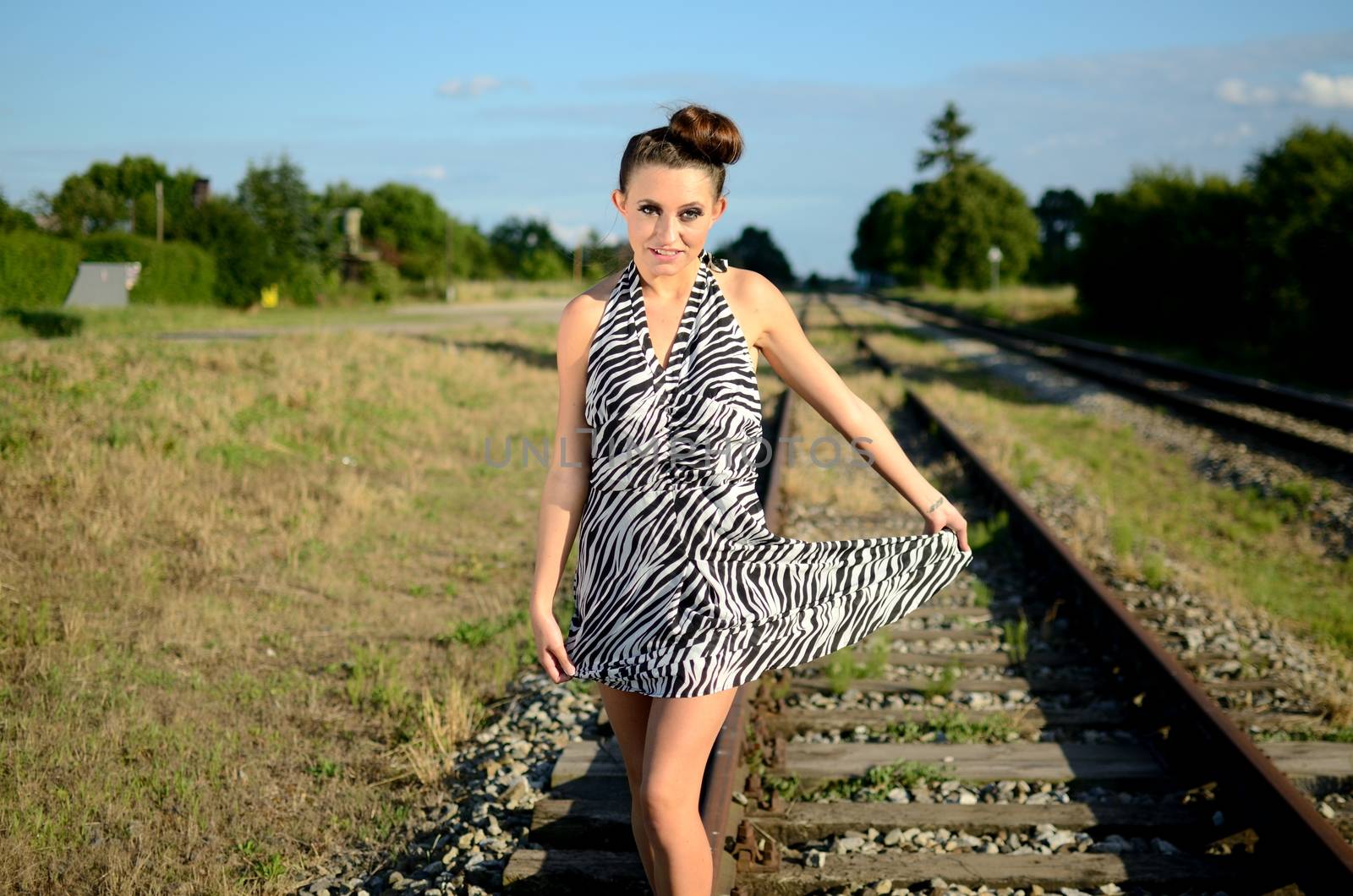 Girl with short skirt walks along railroad. Polish female model with blue sky and green meadows behind her.