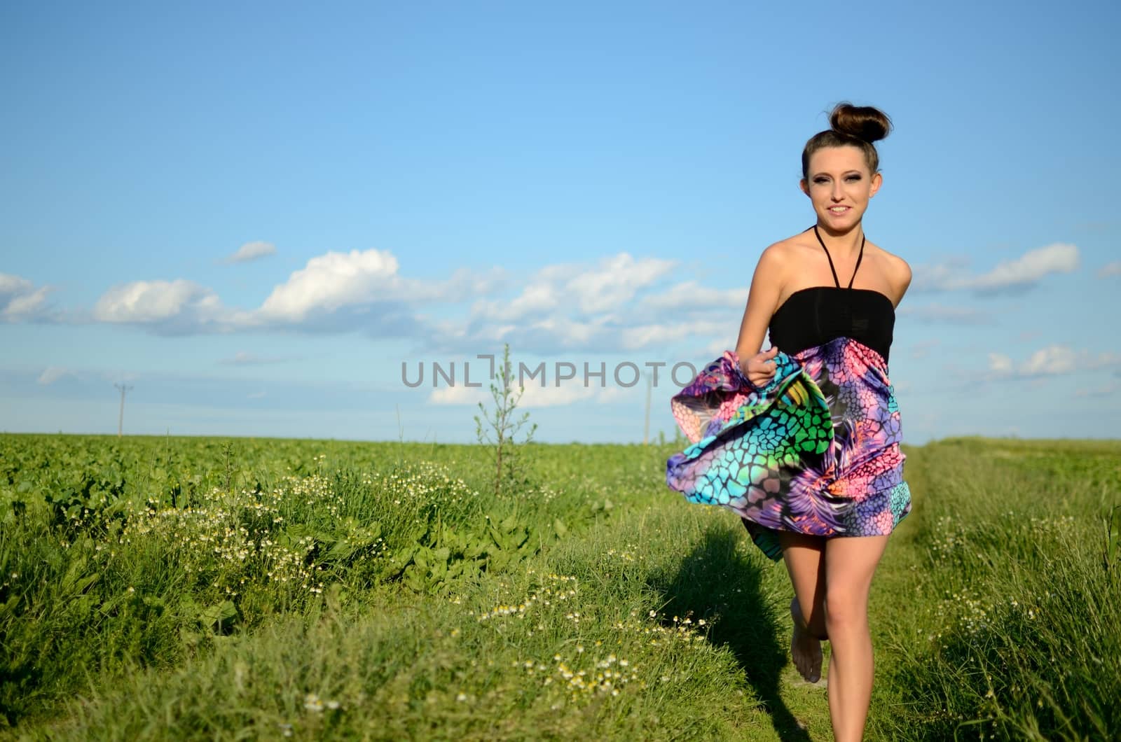 Happy girl runs with colorful dress. Active teenage model from Poland surrounded by green fields and blue sky.