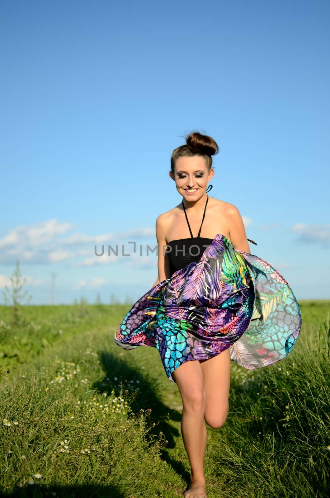 Happy girl runs with colorful dress. Active teenage model from Poland surrounded by green fields and blue sky.
