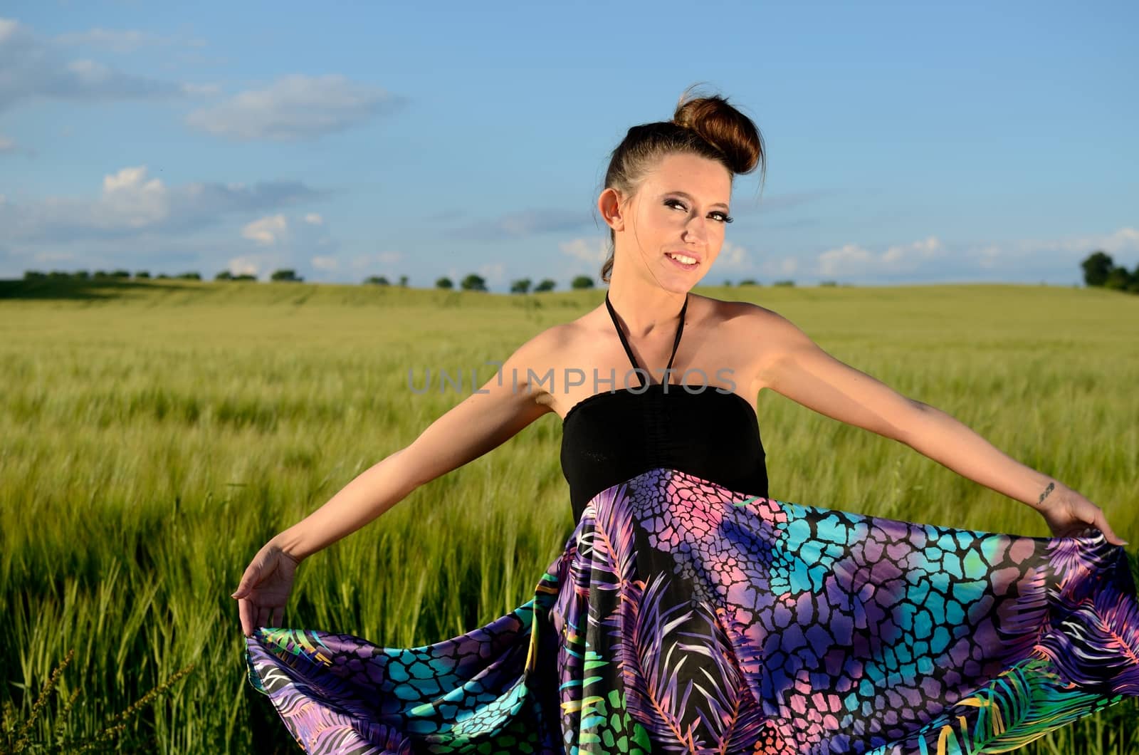Young female model from Poland surrounded by green fields of grains. Girl portrait with colorful skirt.