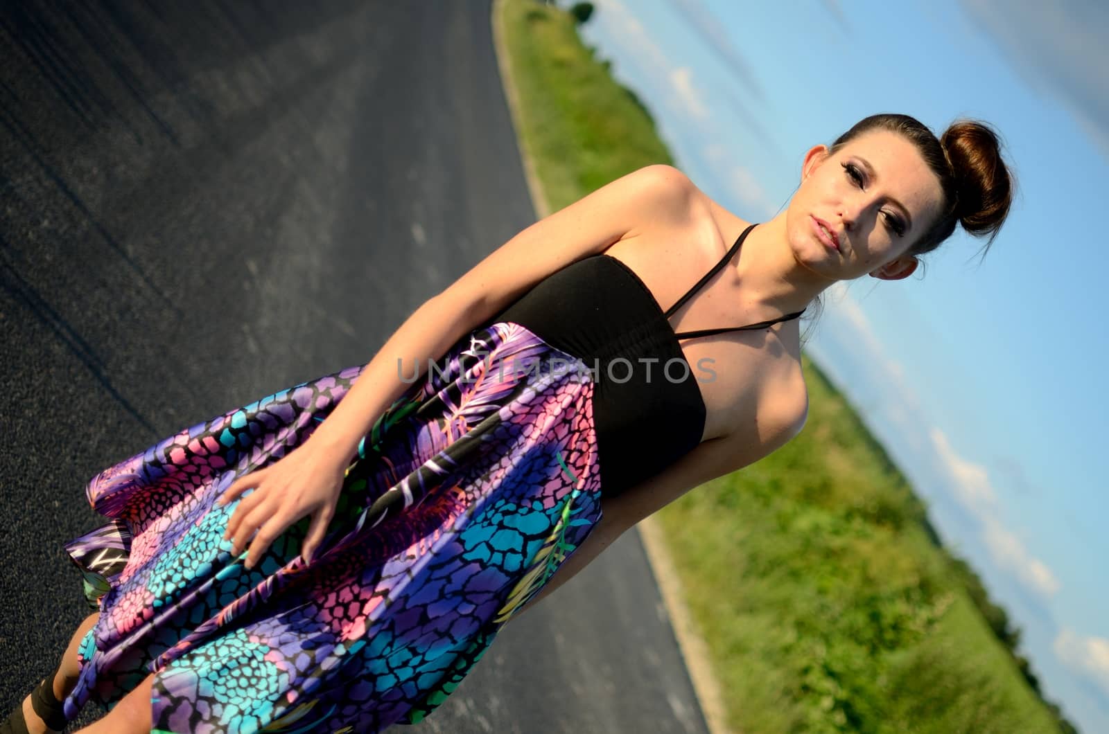 Female model walking on the road with green meadows as background. Young girl from Poland with colorful dress. 