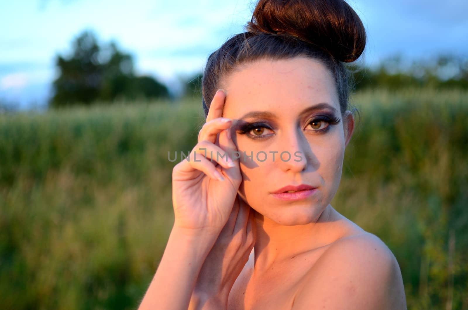 Female model portrait with warm sunset light. Young girl from Poland with blue sky and green meadows as background.