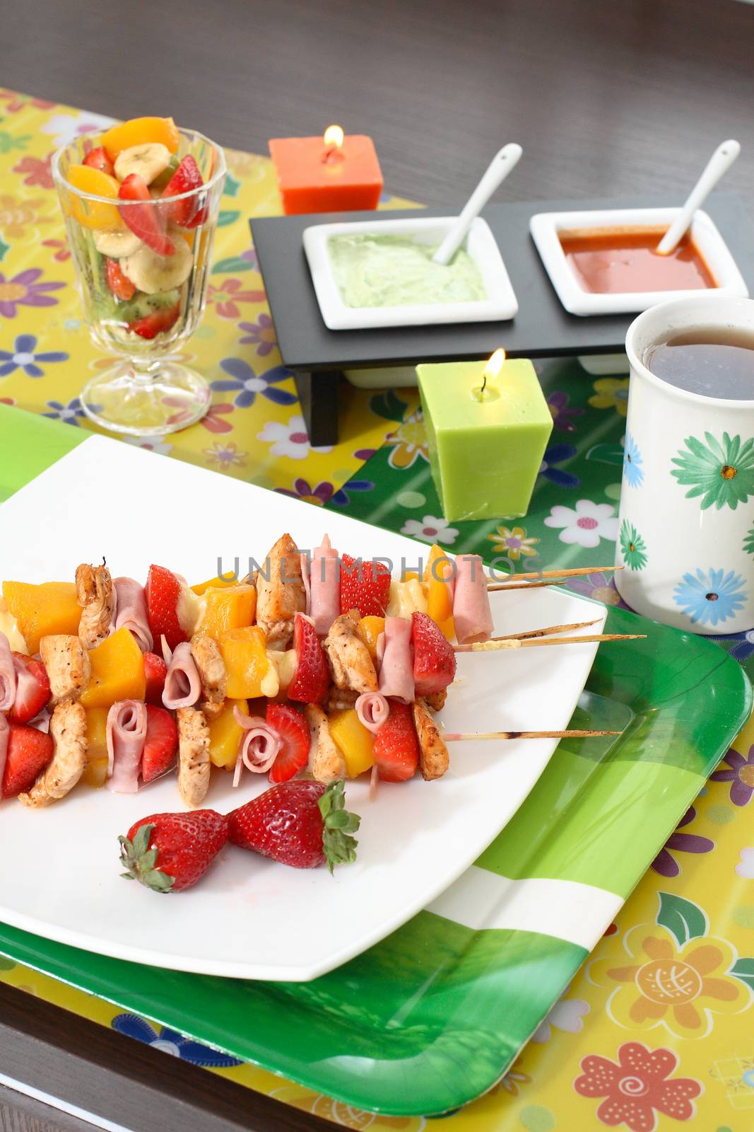 Colorful skewers of chicken, strawberries and pineapple on a white plate