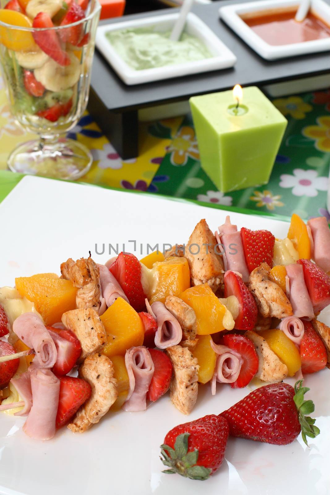 Colorful skewers of chicken, strawberries and pineapple on a white plate
