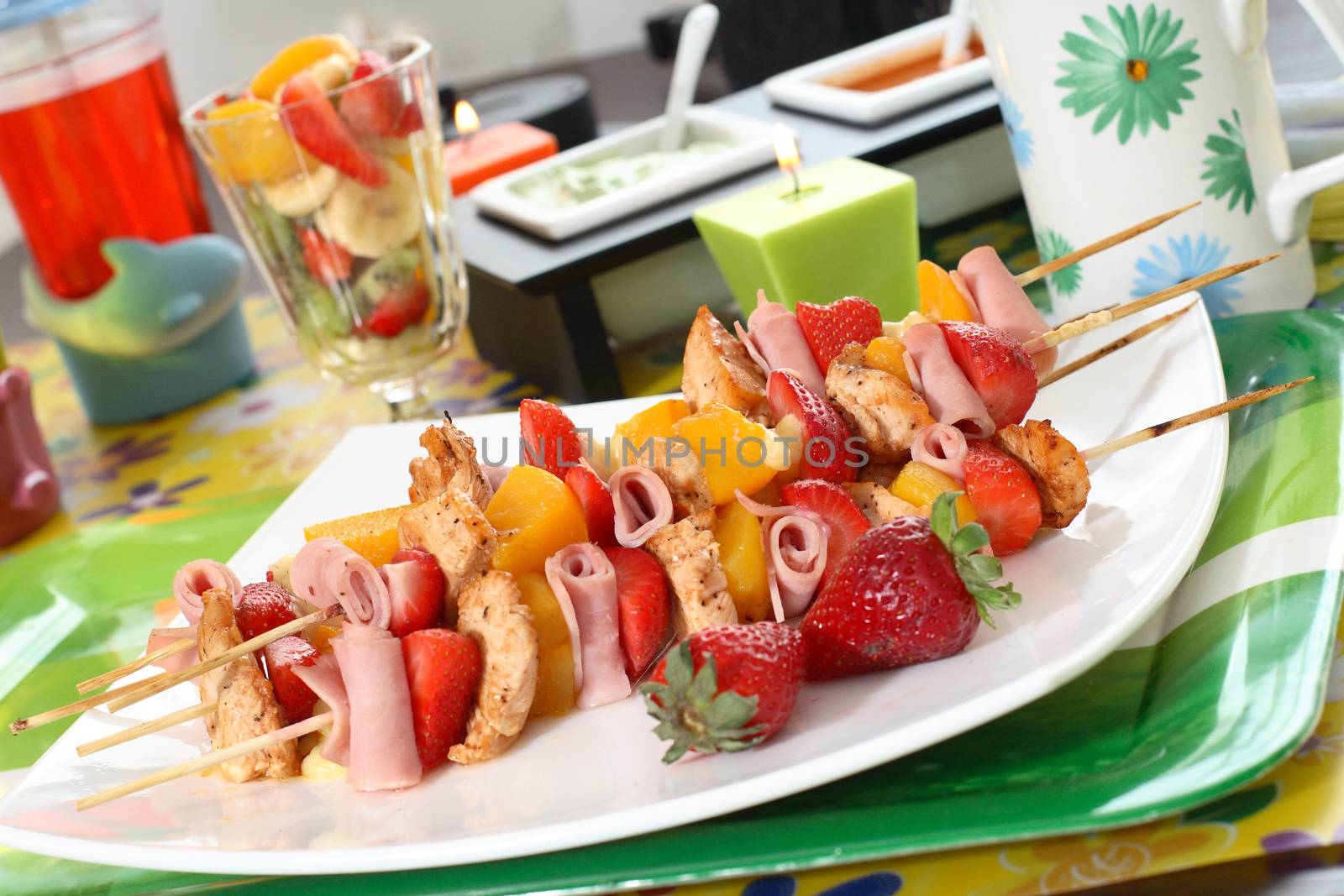 Colorful skewers of chicken, strawberries and pineapple on a white plate