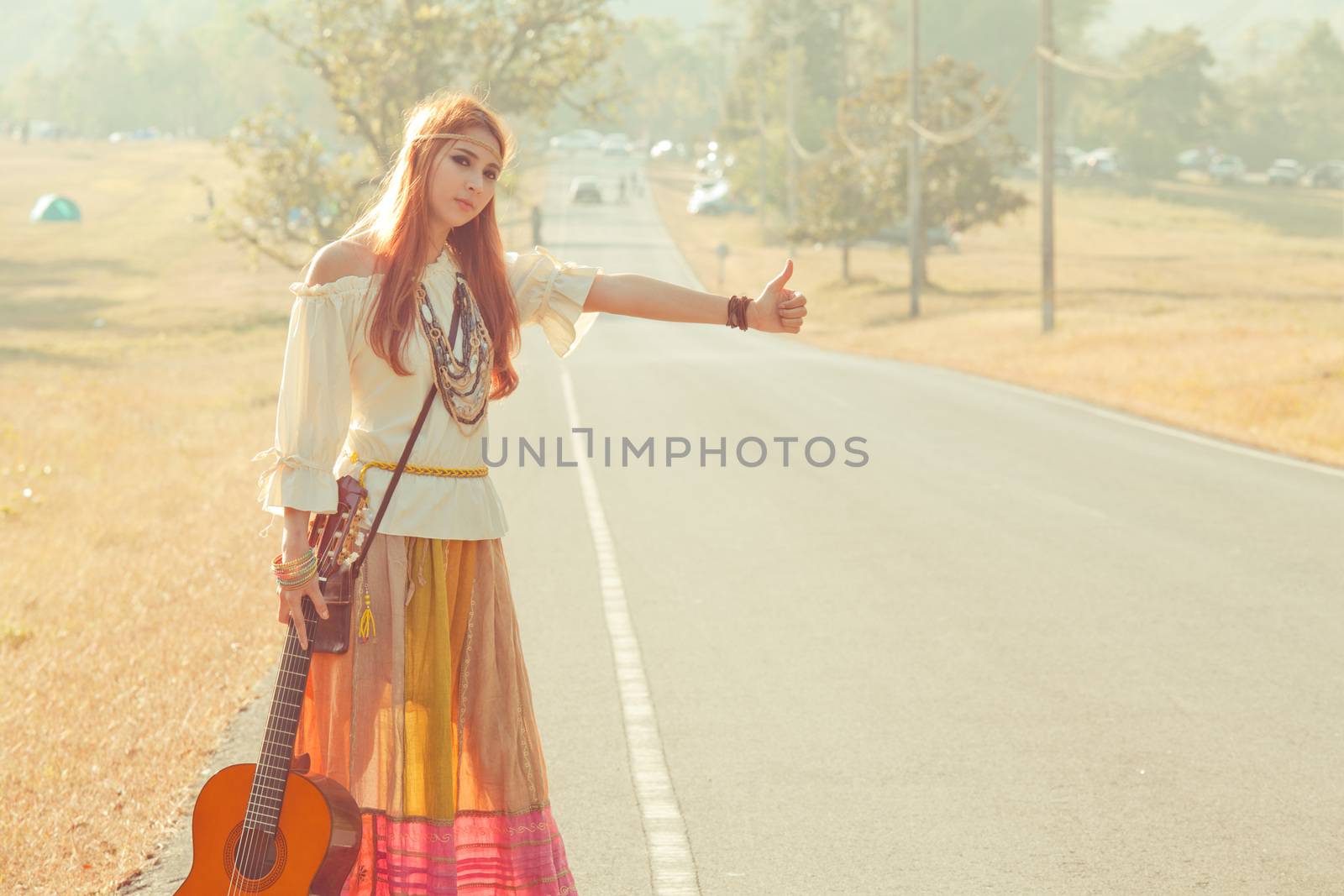 Hippie girl with guitar hitchhiking on countryside road