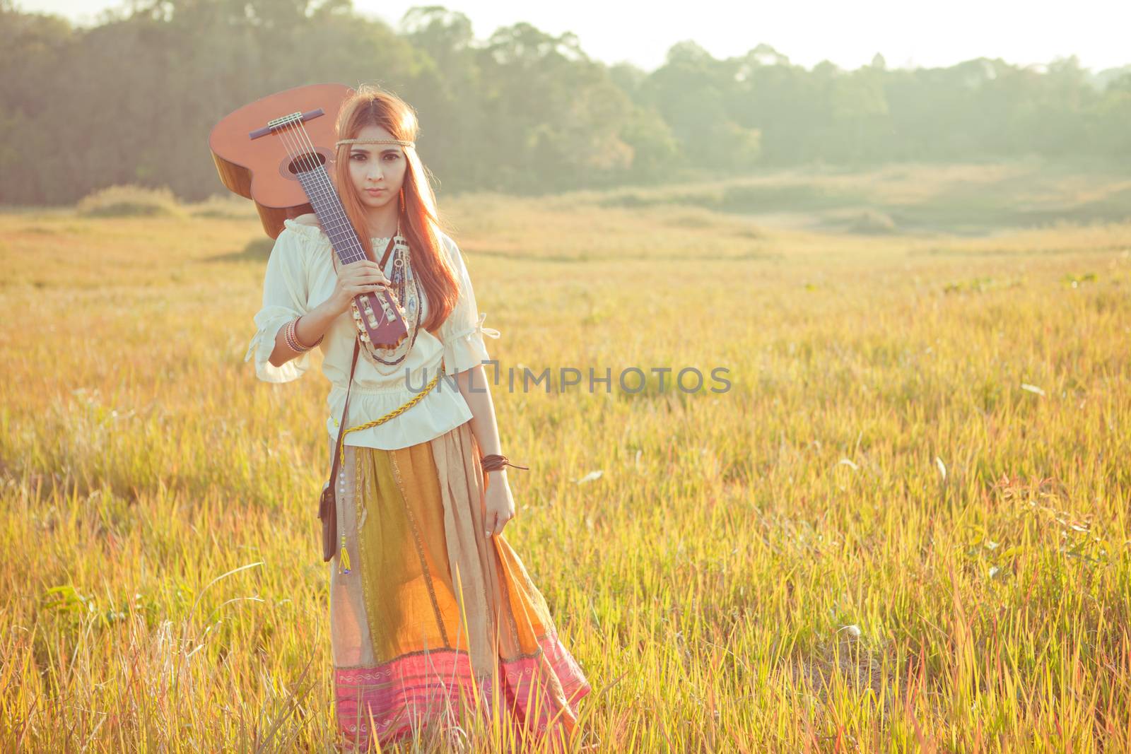 Hippie woman walking in golden field with acoustic guitar