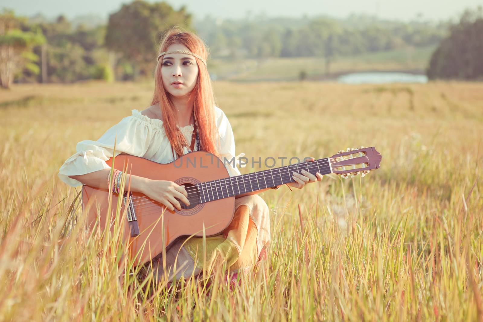Pretty country hippie girl playing guitar on grass
