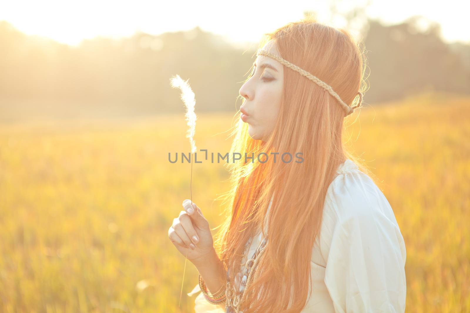 Hippie beautiful woman blowing flower on the golden meadow