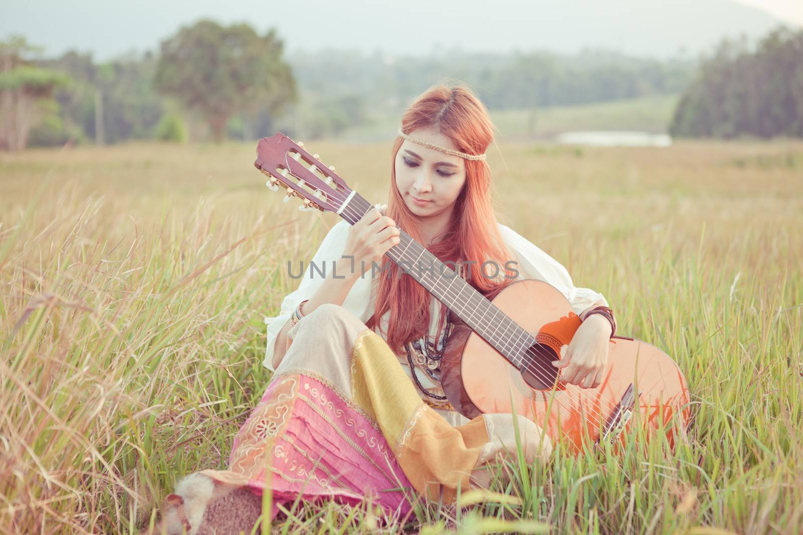 Pretty country hippie girl playing guitar on grass